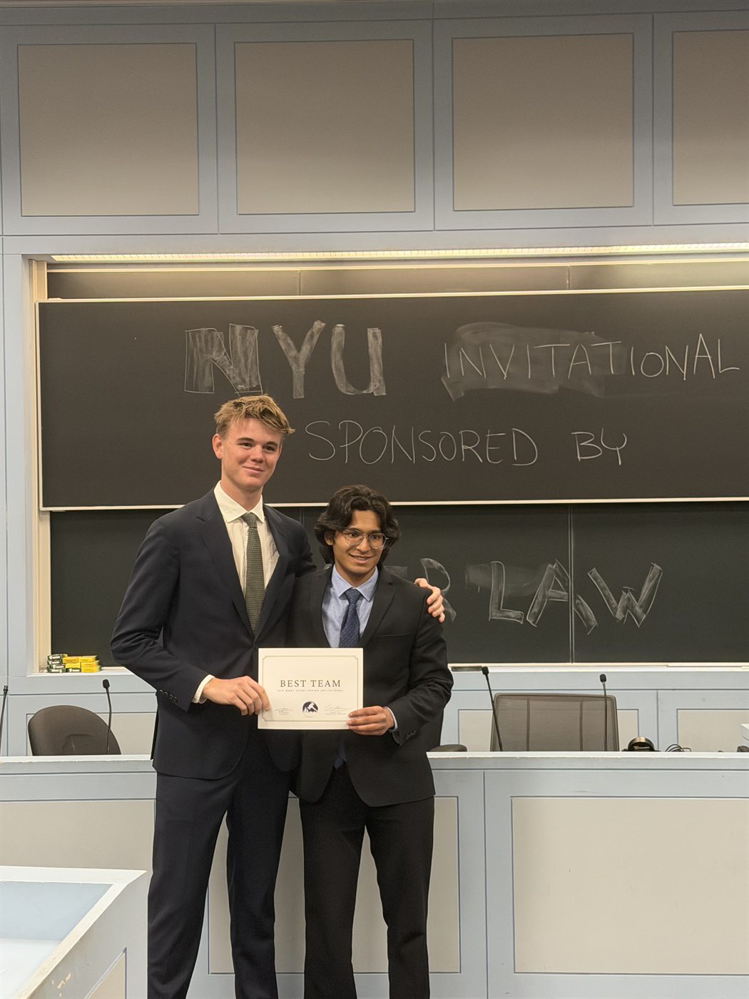 Ben Brown and Muhammed Khan holding the Best Team certificate in front of a chalkboard reading NYU Invitational.