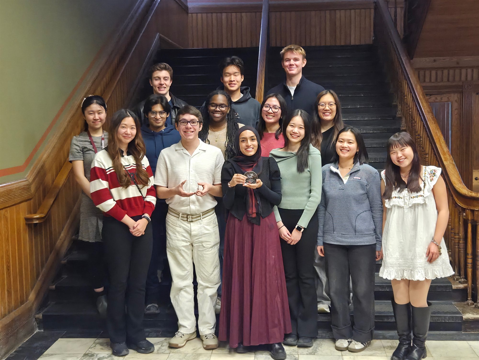 Members of Harvard Undergraduate Moot Court gathered on a staircase with competition trophies.